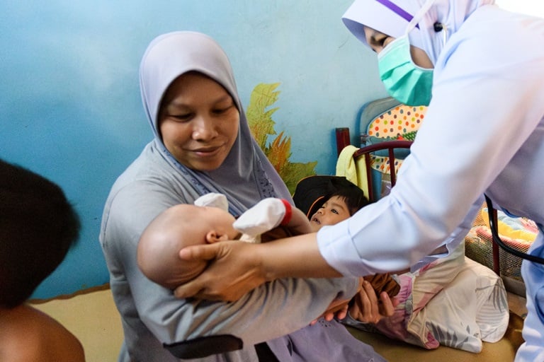 A mother holds her infant while a nurse gives the baby a check up